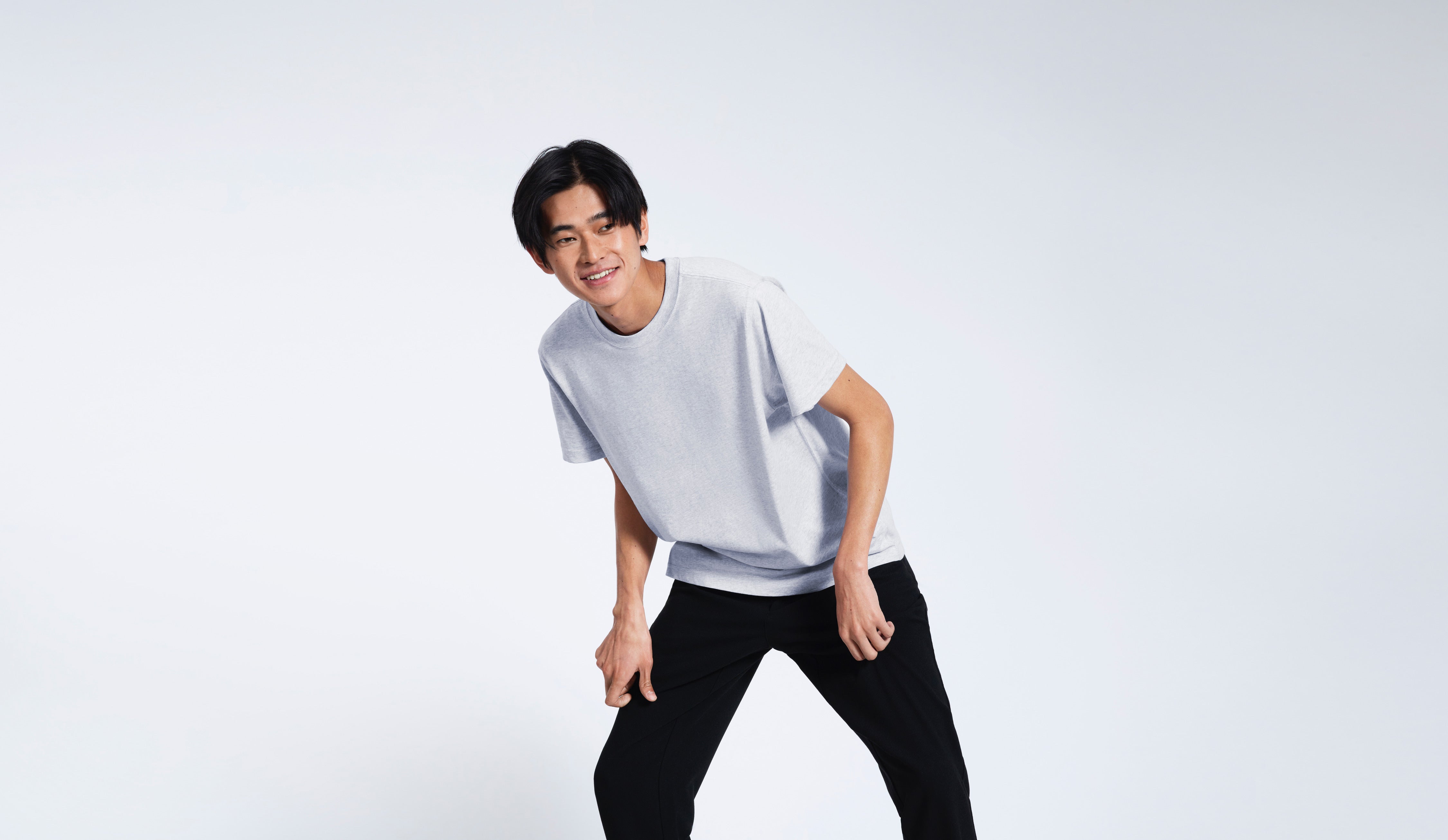 A man leaning over slightly, smiling, modelling a plain short sleeve grey organic cotton t shirt.