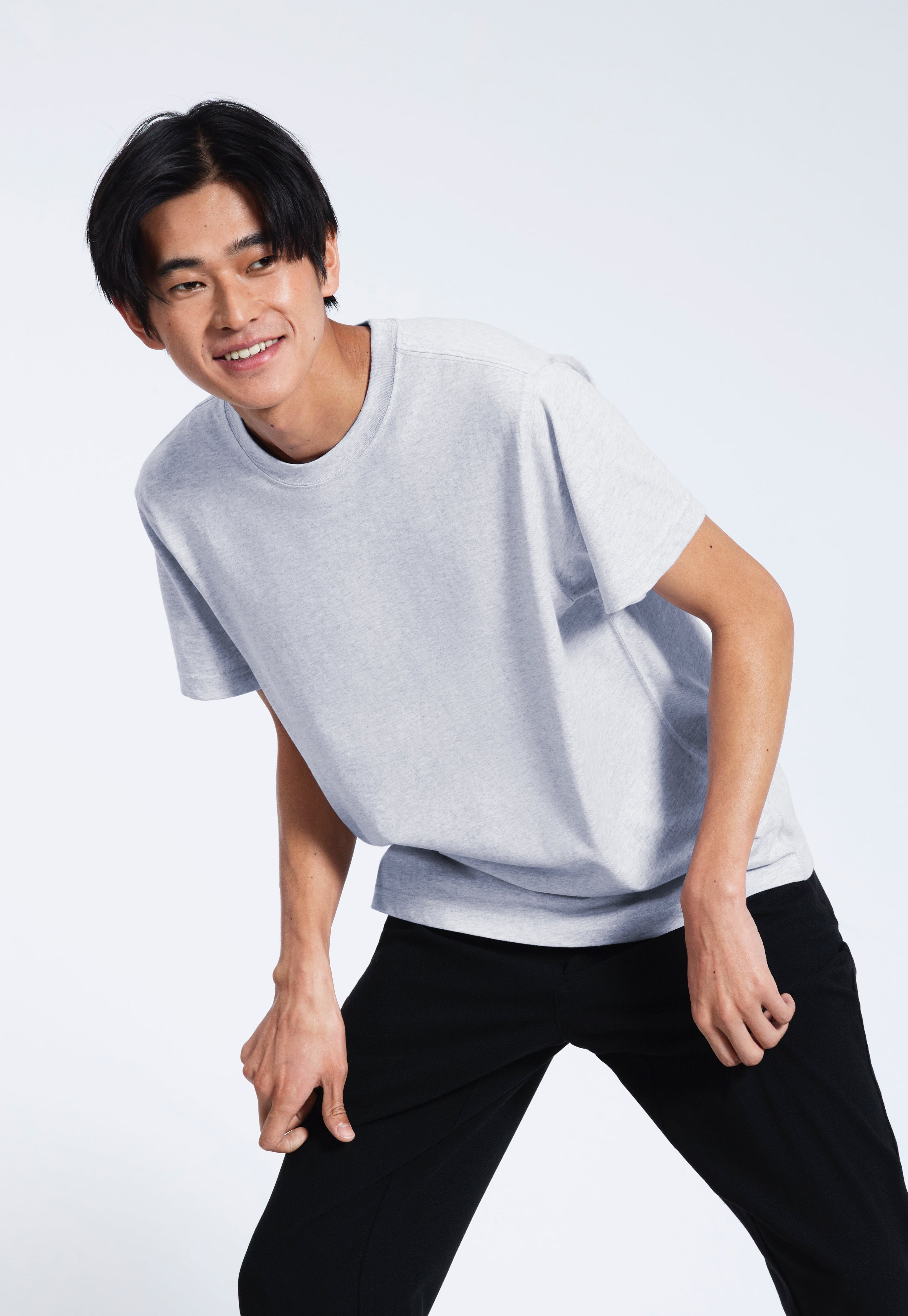 A man leaning over slightly, smiling, modelling a plain short sleeve grey organic cotton t shirt.